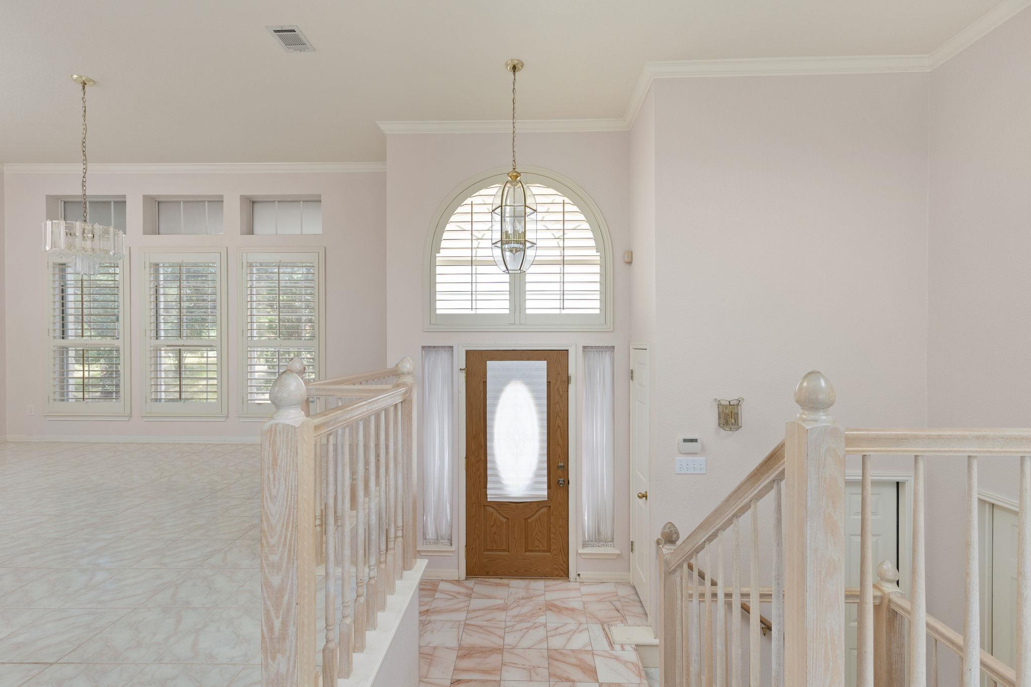 Two-story entry foyer with marble tile, a wood front door, arched window, and staircase railings.
