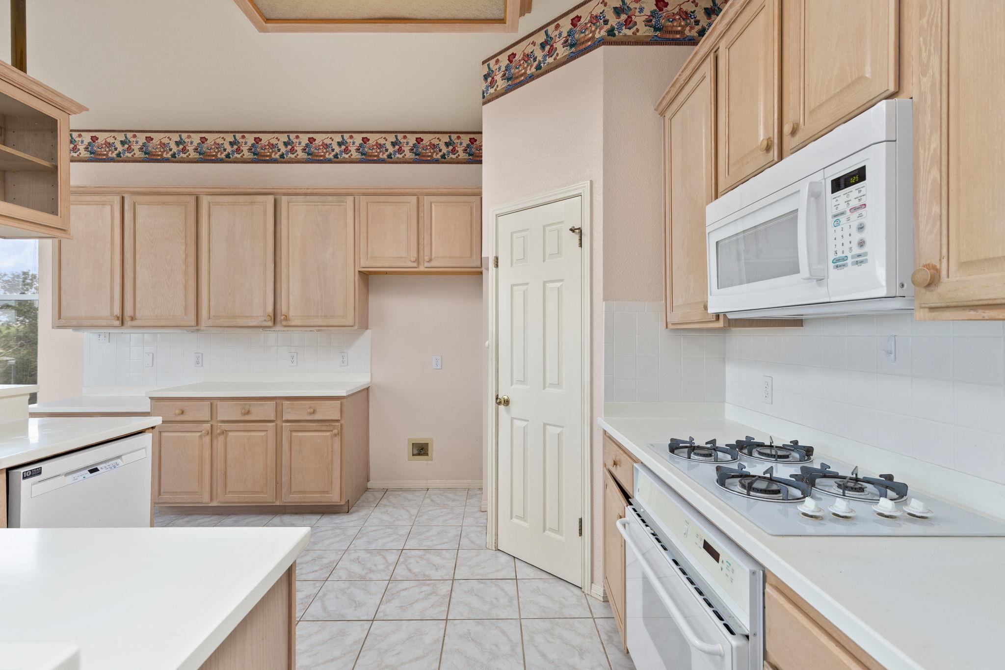 Kitchen with light wood cabinets, white tile counters, and a gas cooktop beneath a built-in microwave.