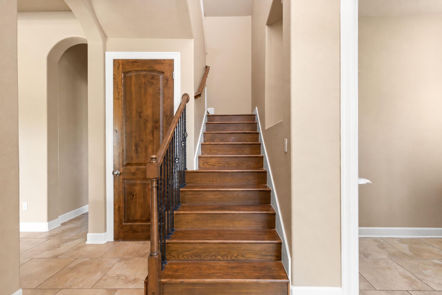 Wooden staircase with black metal balusters beside a matching wood door.