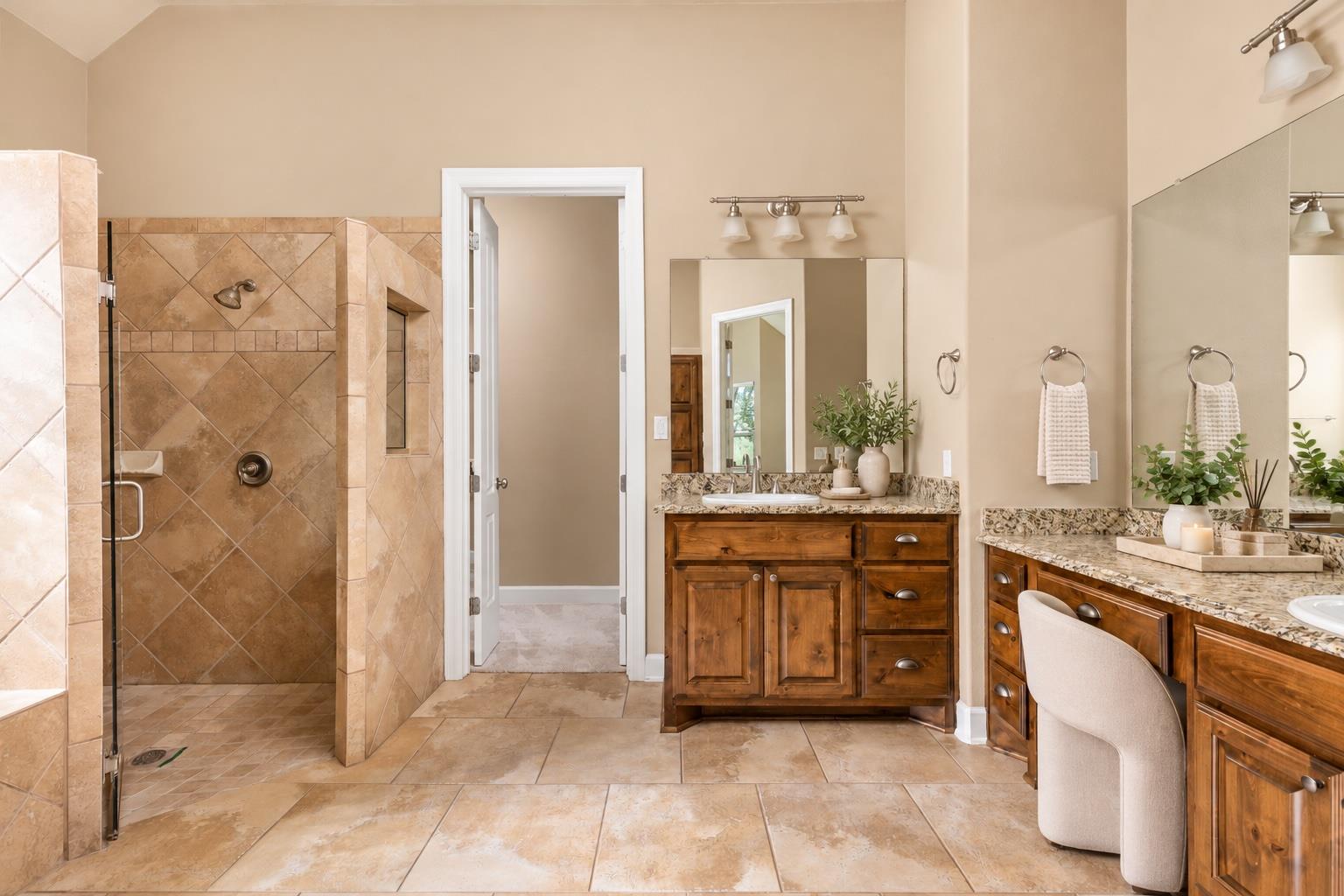 Bathroom with a tiled walk-in shower and two wood vanities with stone countertops.