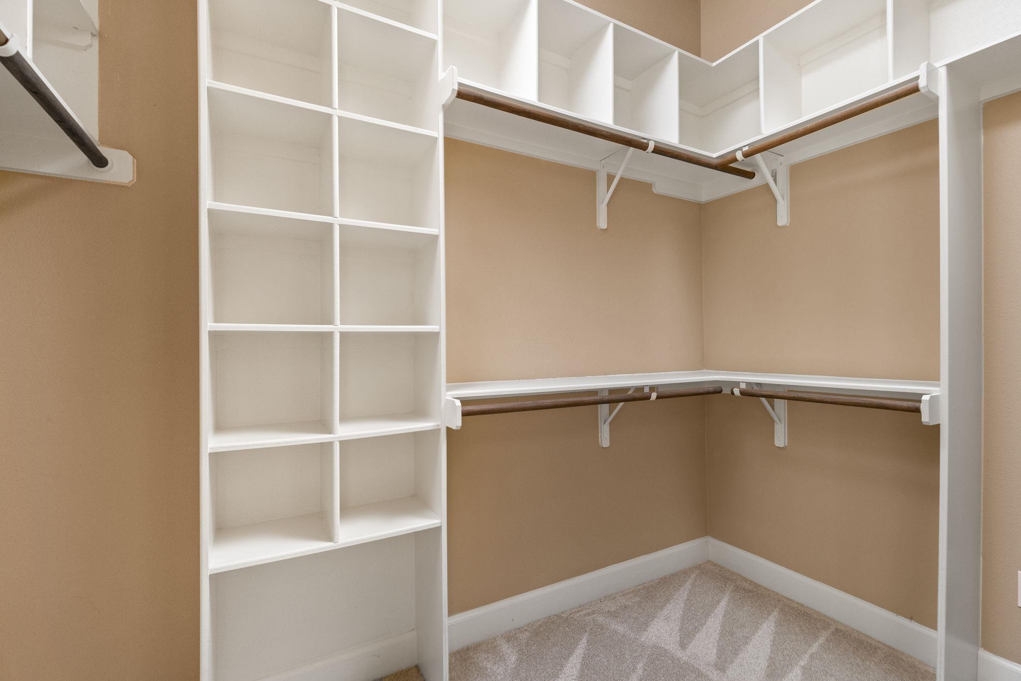 Walk-in closet with white built-in shelves and wraparound hanging rods.