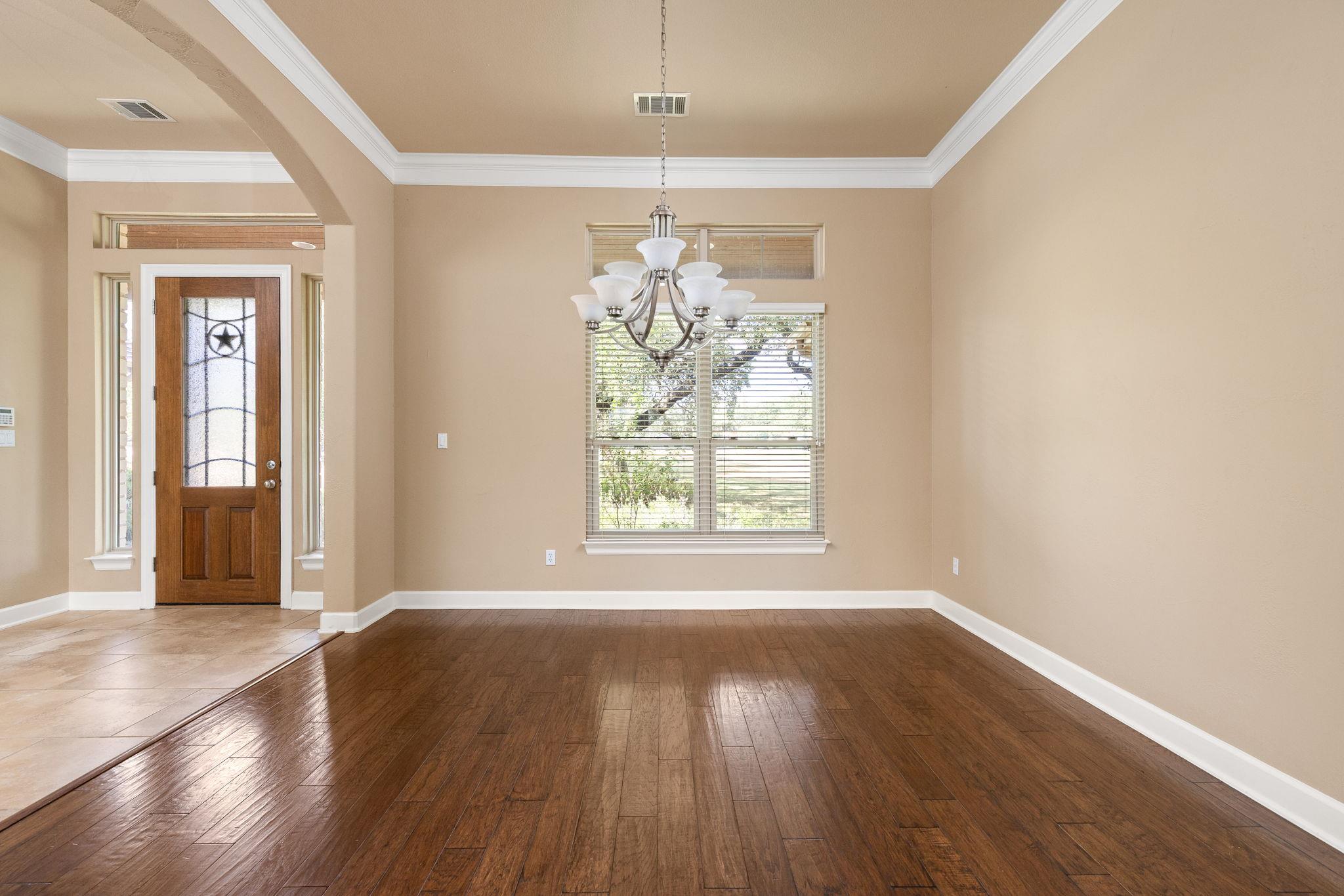 Empty dining area with a chandelier, dark wood floors, and a window beside the tiled entry foyer.