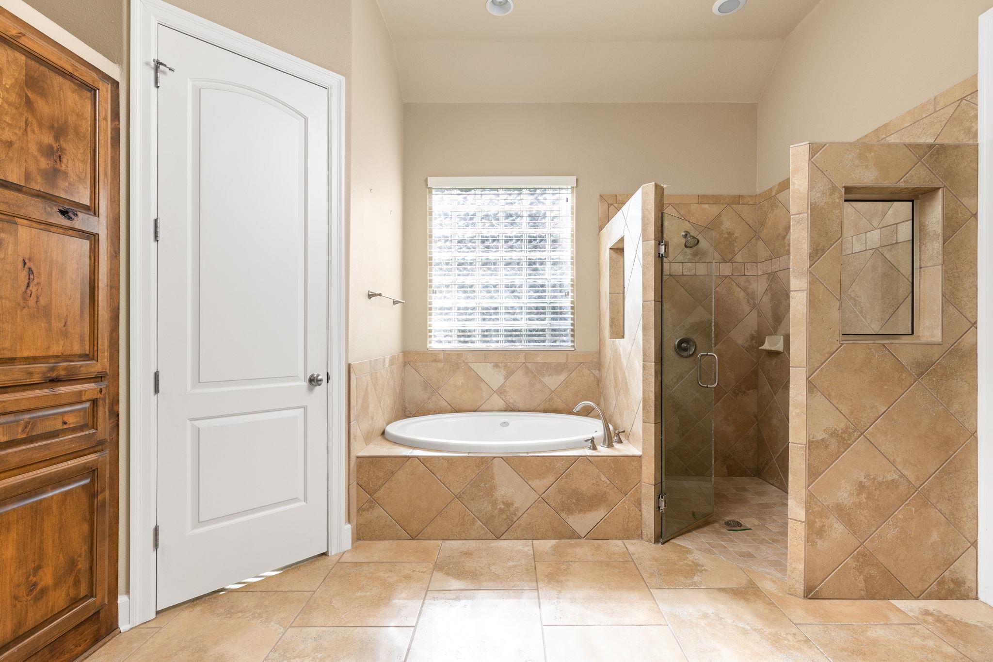Bathroom with a tiled soaking tub beneath a window and a glass-enclosed walk-in shower.