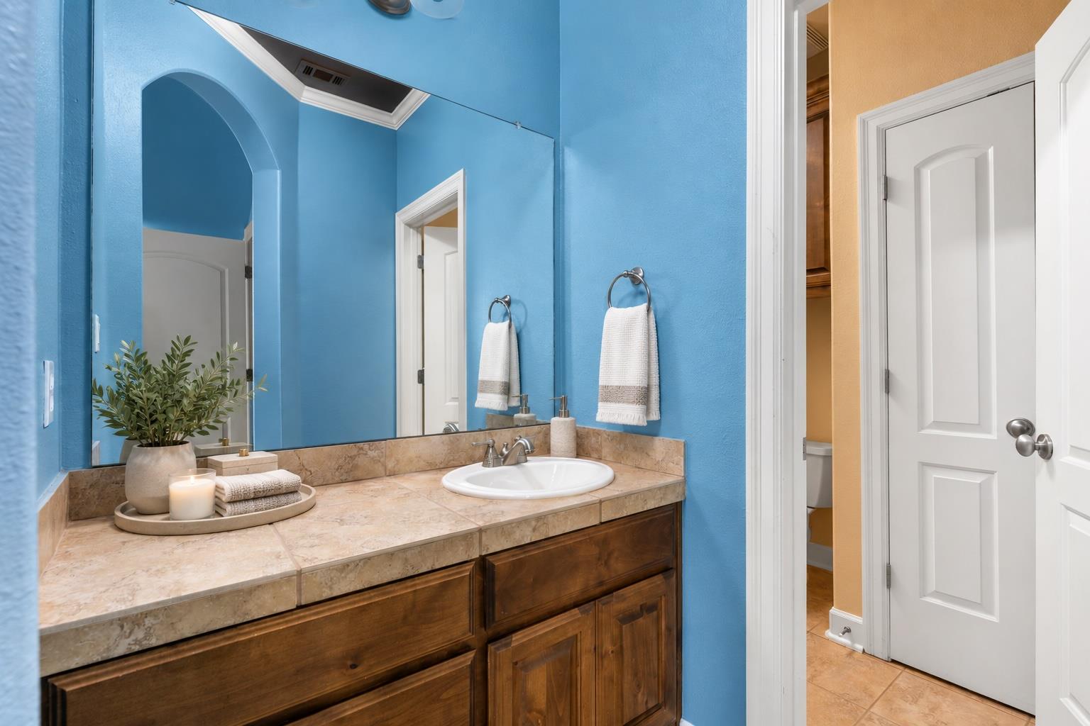 Bathroom with blue walls, a long wood vanity, tan stone countertop, and large mirror.