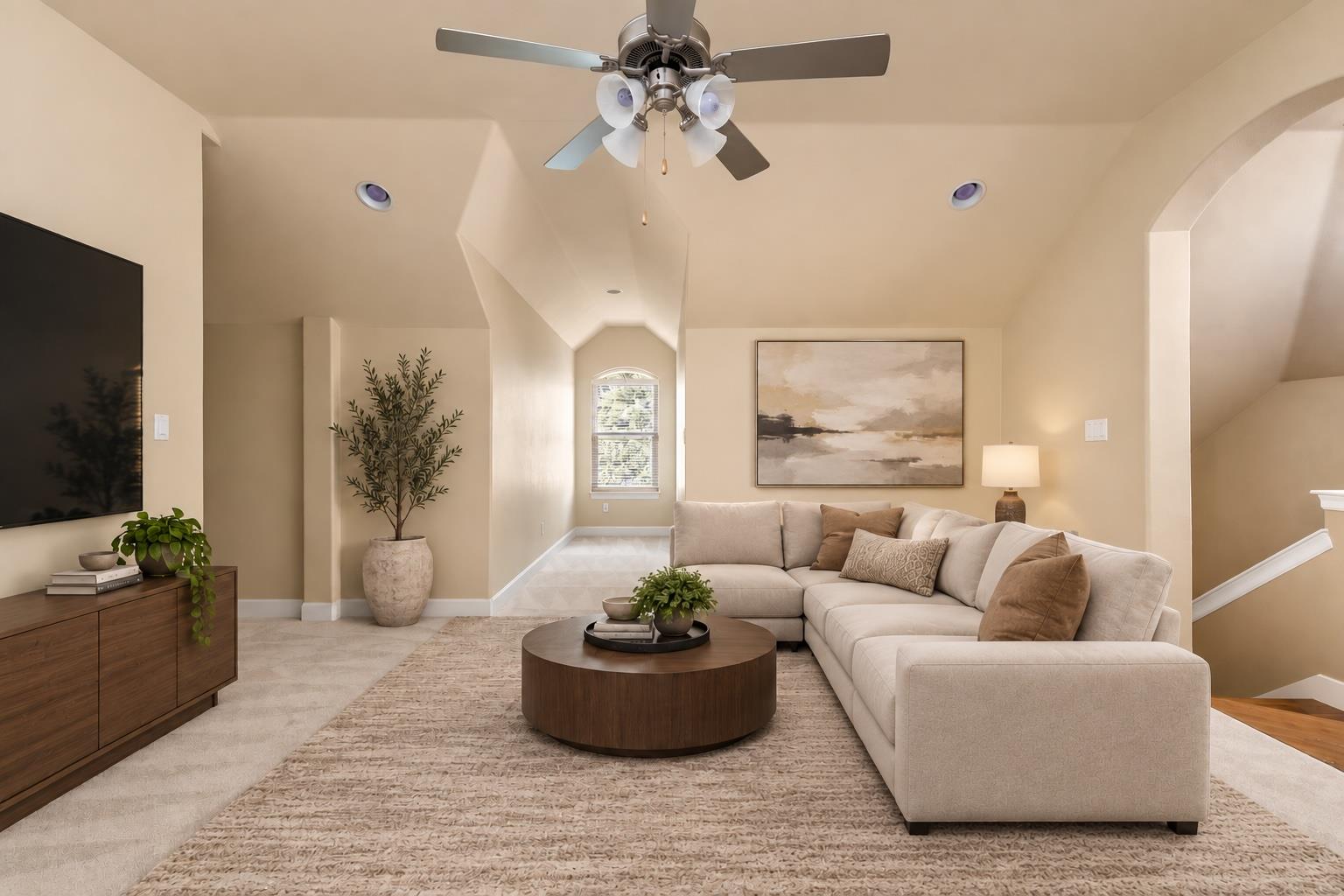 Staged living room with a cream sectional, round wood coffee table, ceiling fan, and arched window.