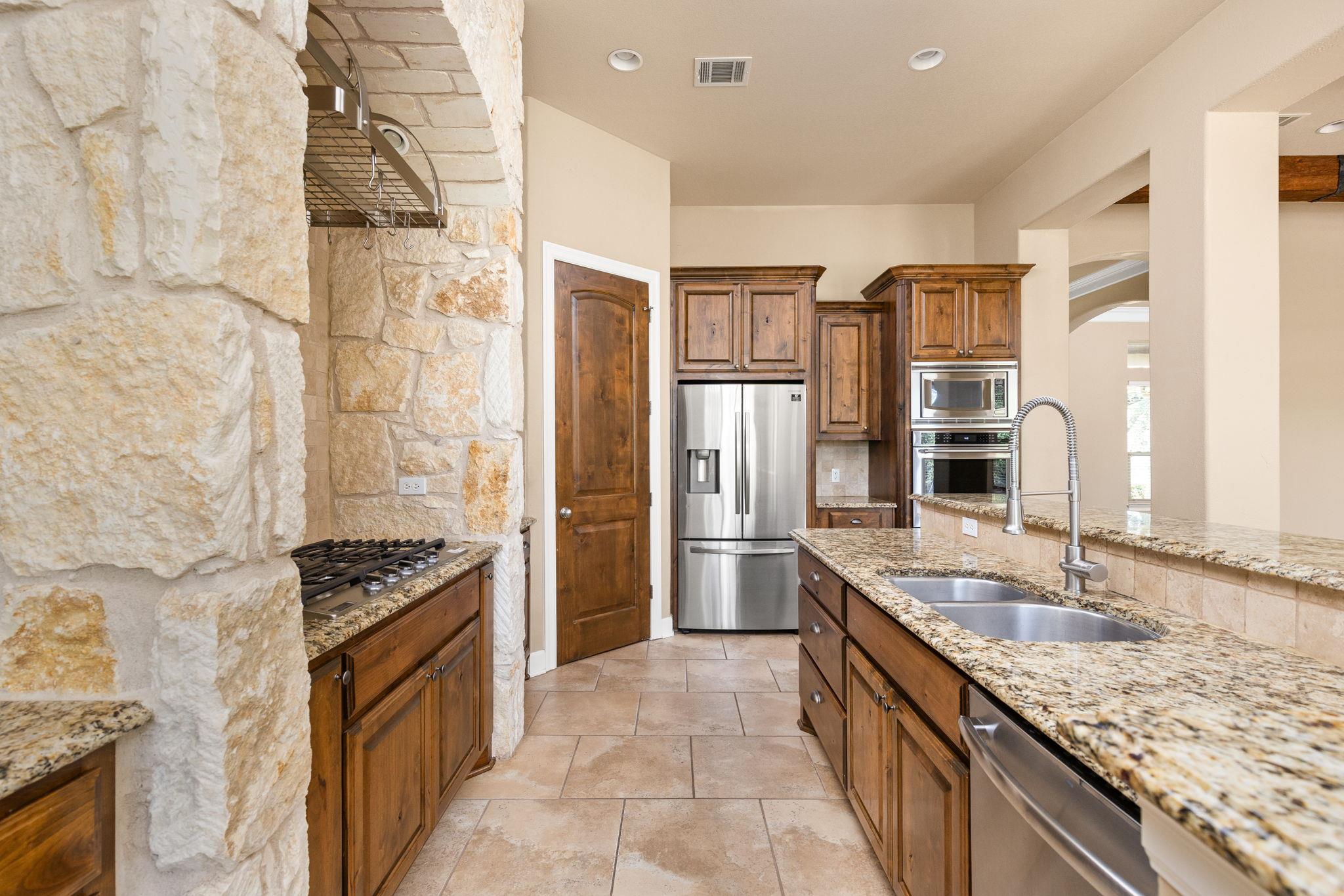Kitchen with dark wood cabinets, granite counters, stainless appliances, and a prominent stone column.