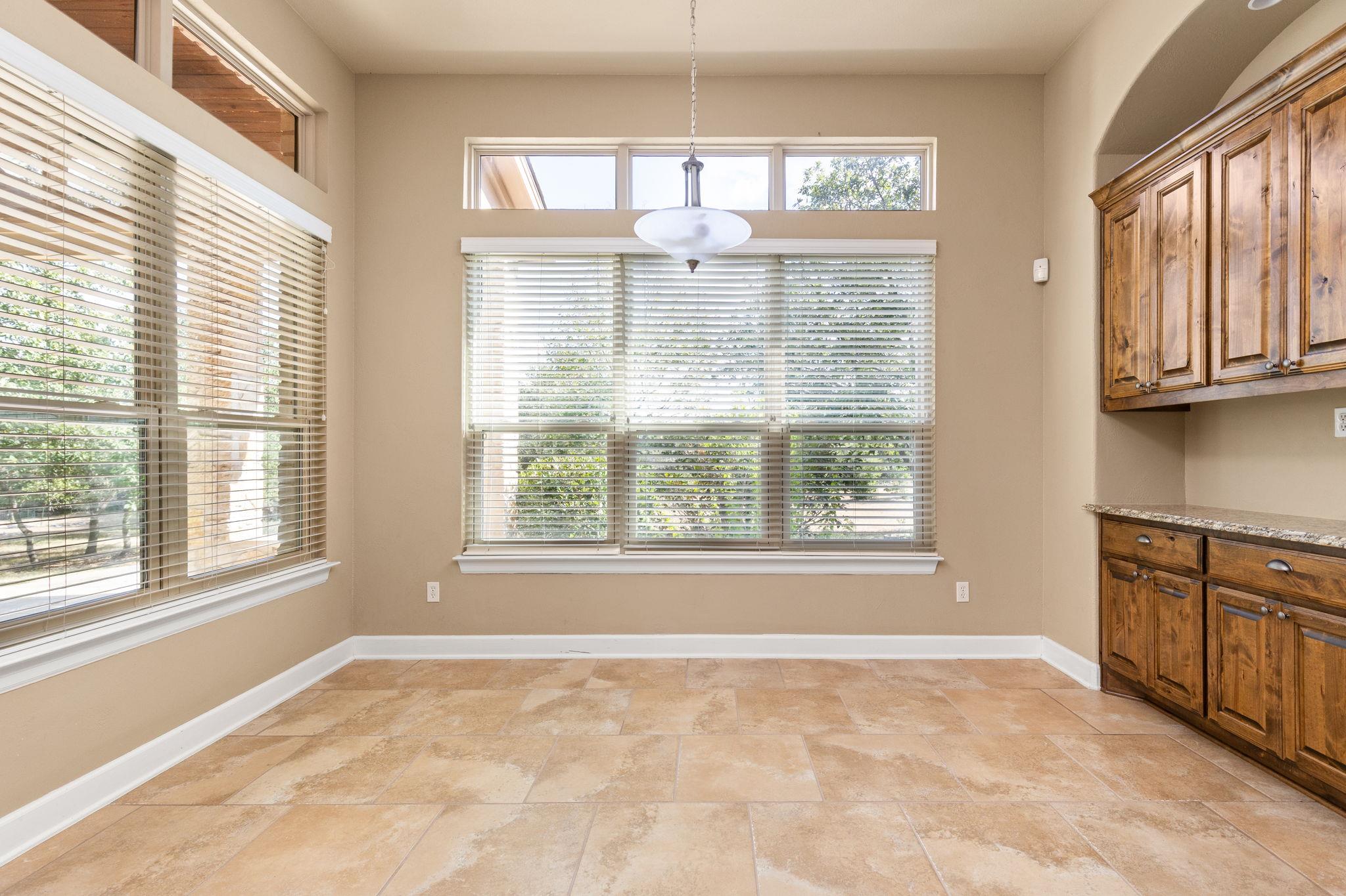 Empty dining nook with tan tile floors, broad windows, and rustic wood cabinetry.