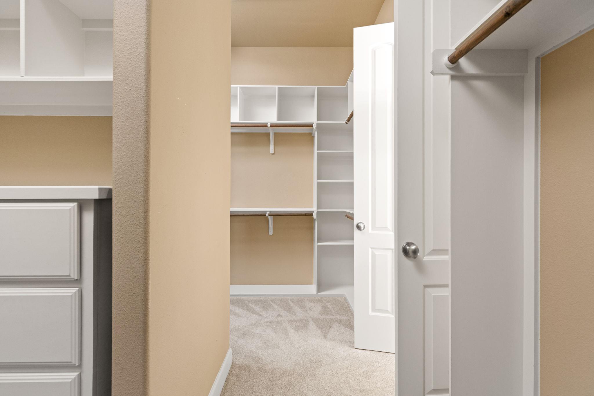Walk-in closet with built-in shelving, hanging rods, and carpeted floor.