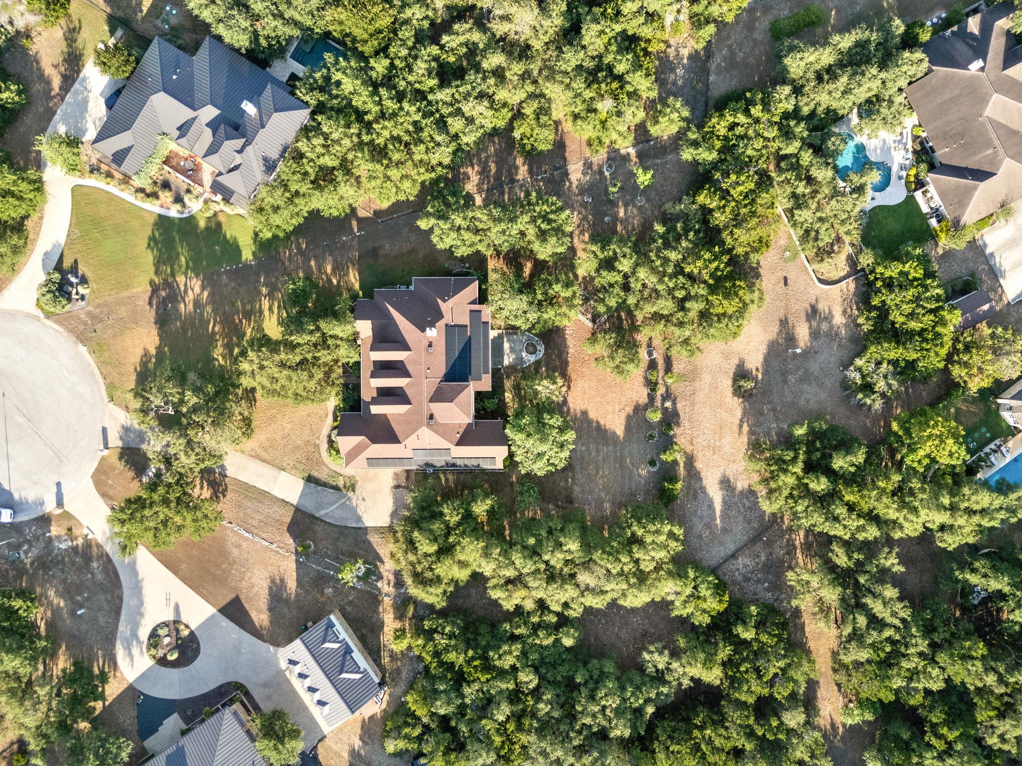 Aerial view of a house amid mature trees, with a broad driveway and neighboring homes.