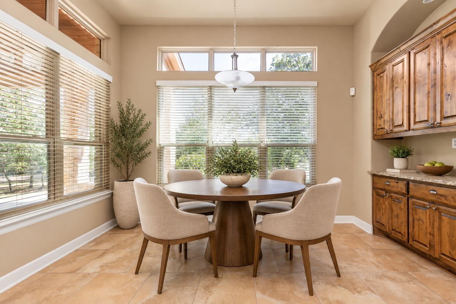 Dining area with a round wood table, upholstered chairs, large windows, and wood cabinetry.