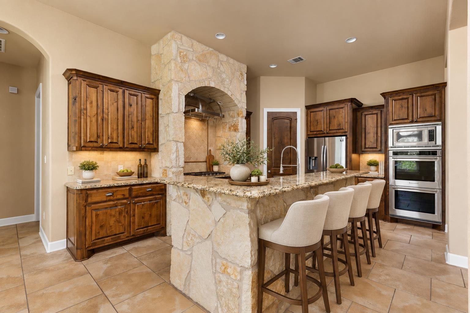 Kitchen with a granite island, stone column, dark wood cabinetry, and stainless steel appliances.
