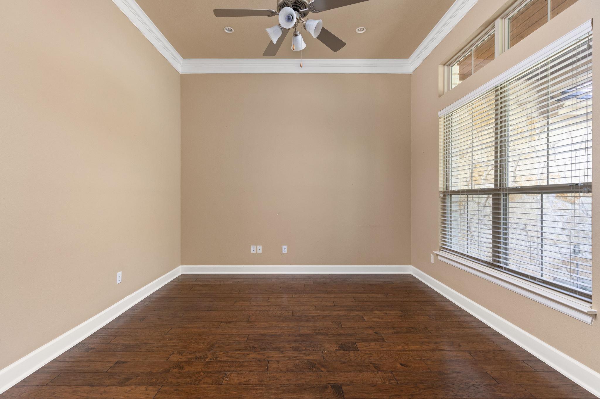 Empty room with dark wood floors, a ceiling fan, and large windows with blinds.