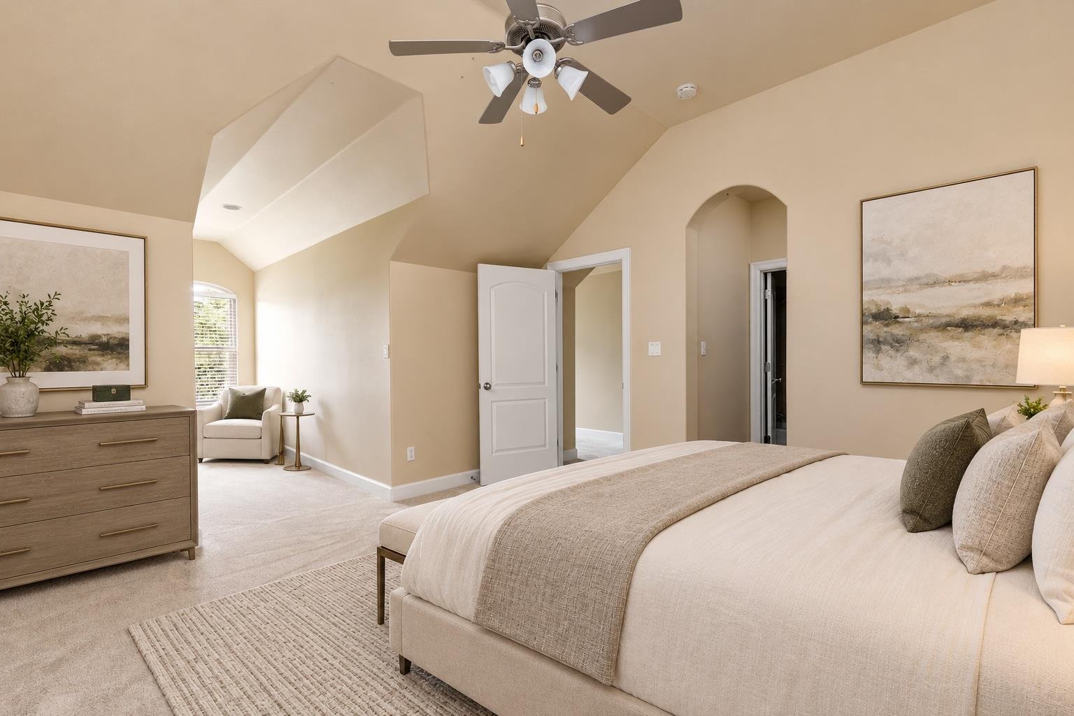 Staged bedroom with an upholstered bed beneath a vaulted ceiling and ceiling fan.