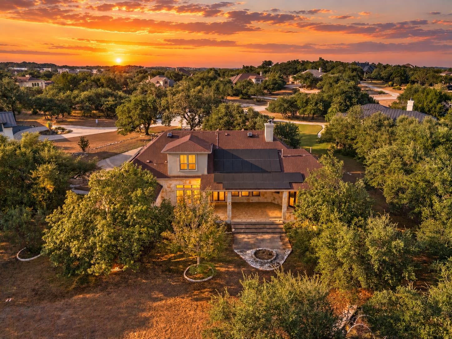 Aerial view of a stone home with rooftop solar panels and a covered patio at sunset.