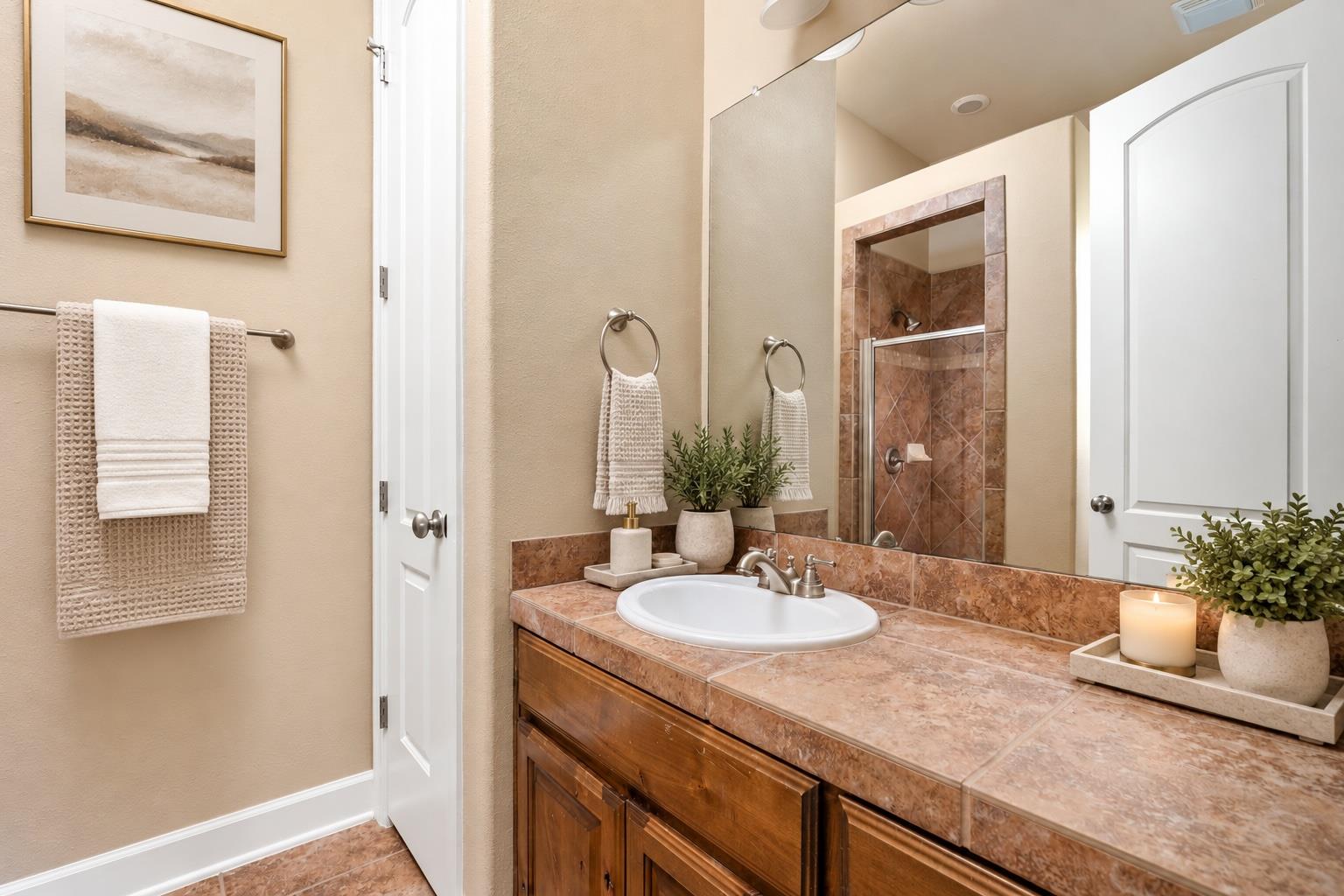 Bathroom with a wood vanity, pink-toned stone countertop, large mirror, and tiled glass-door shower.