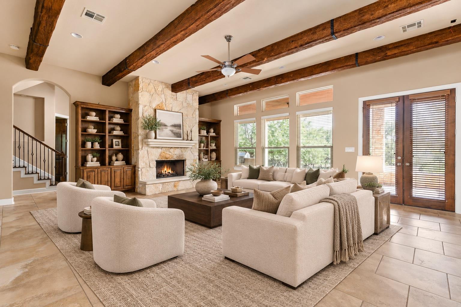 Living room with exposed wood beams, a stone fireplace, and neutral seating around a coffee table.