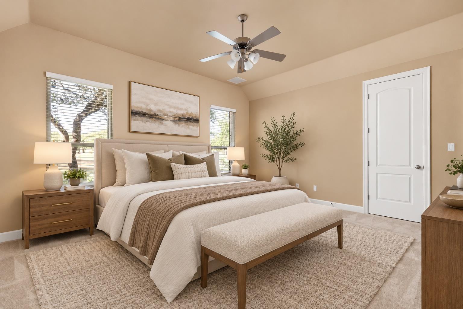 Staged bedroom with a neutral upholstered bed, matching bench, wood nightstands, and windows with blinds.