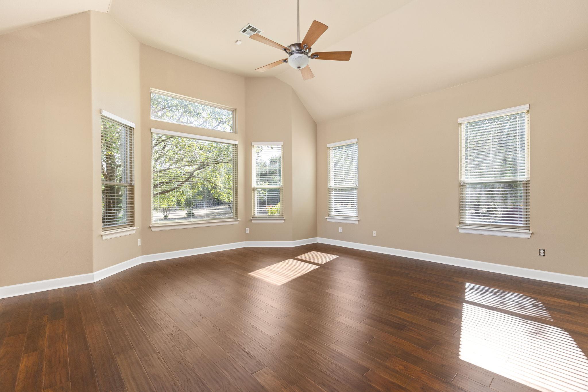 Empty room with vaulted ceiling, dark wood floors, ceiling fan, and multiple windows.