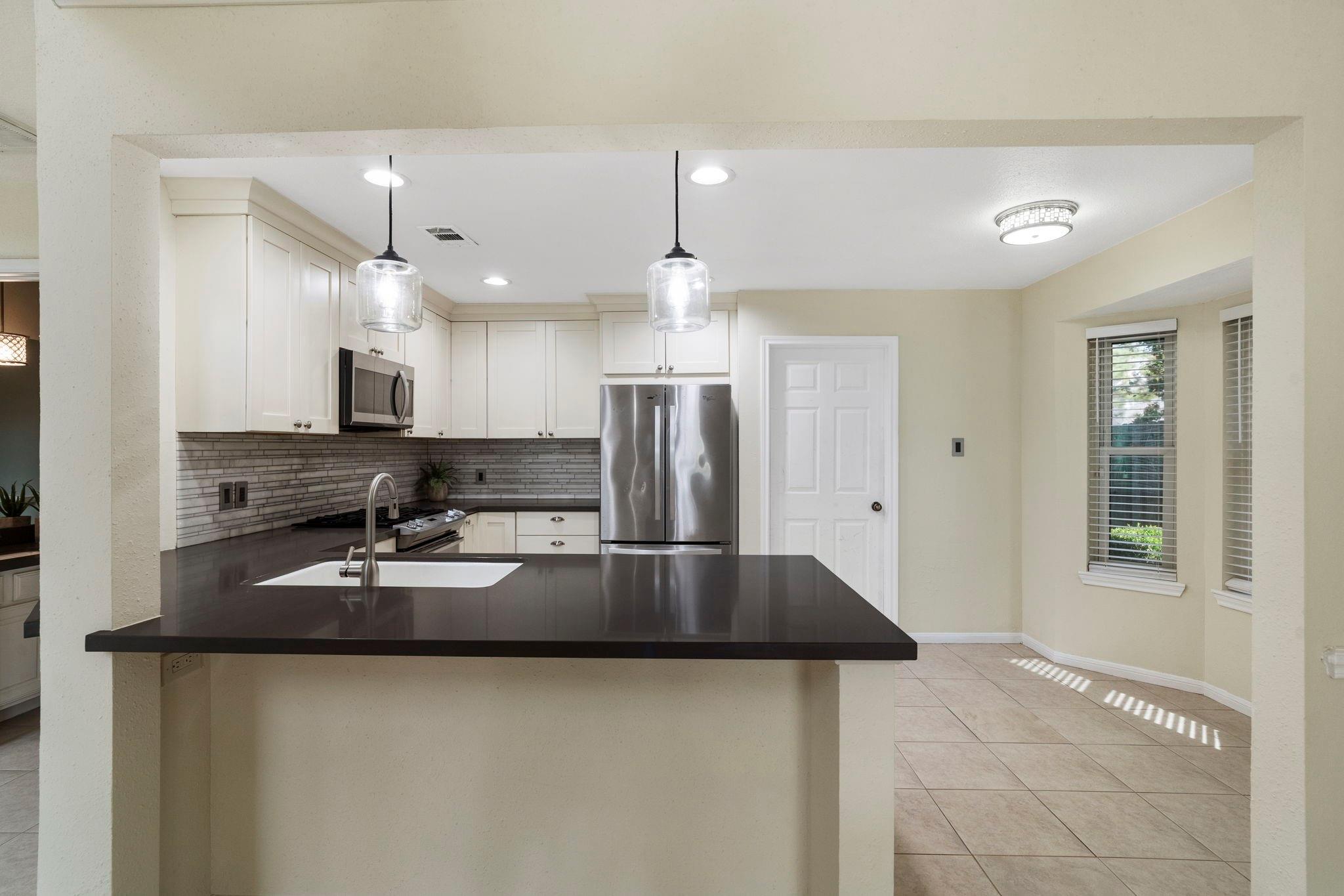 Kitchen with a dark stone island, white cabinets, stainless steel appliances, and tiled backsplash.