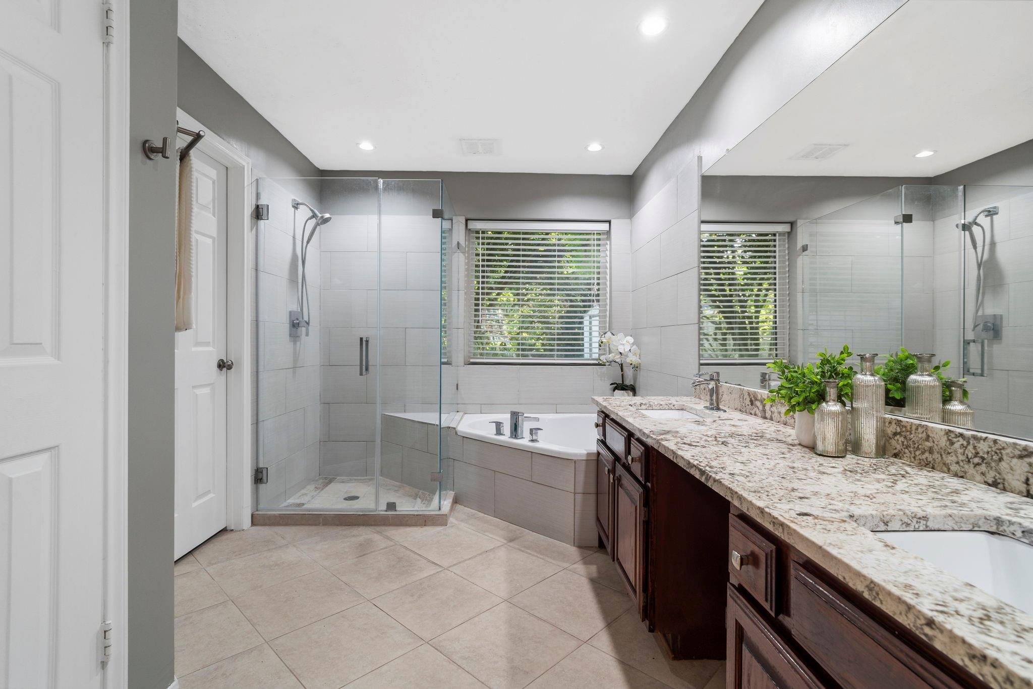 Bathroom with a glass walk-in shower, corner soaking tub, and granite double vanity.
