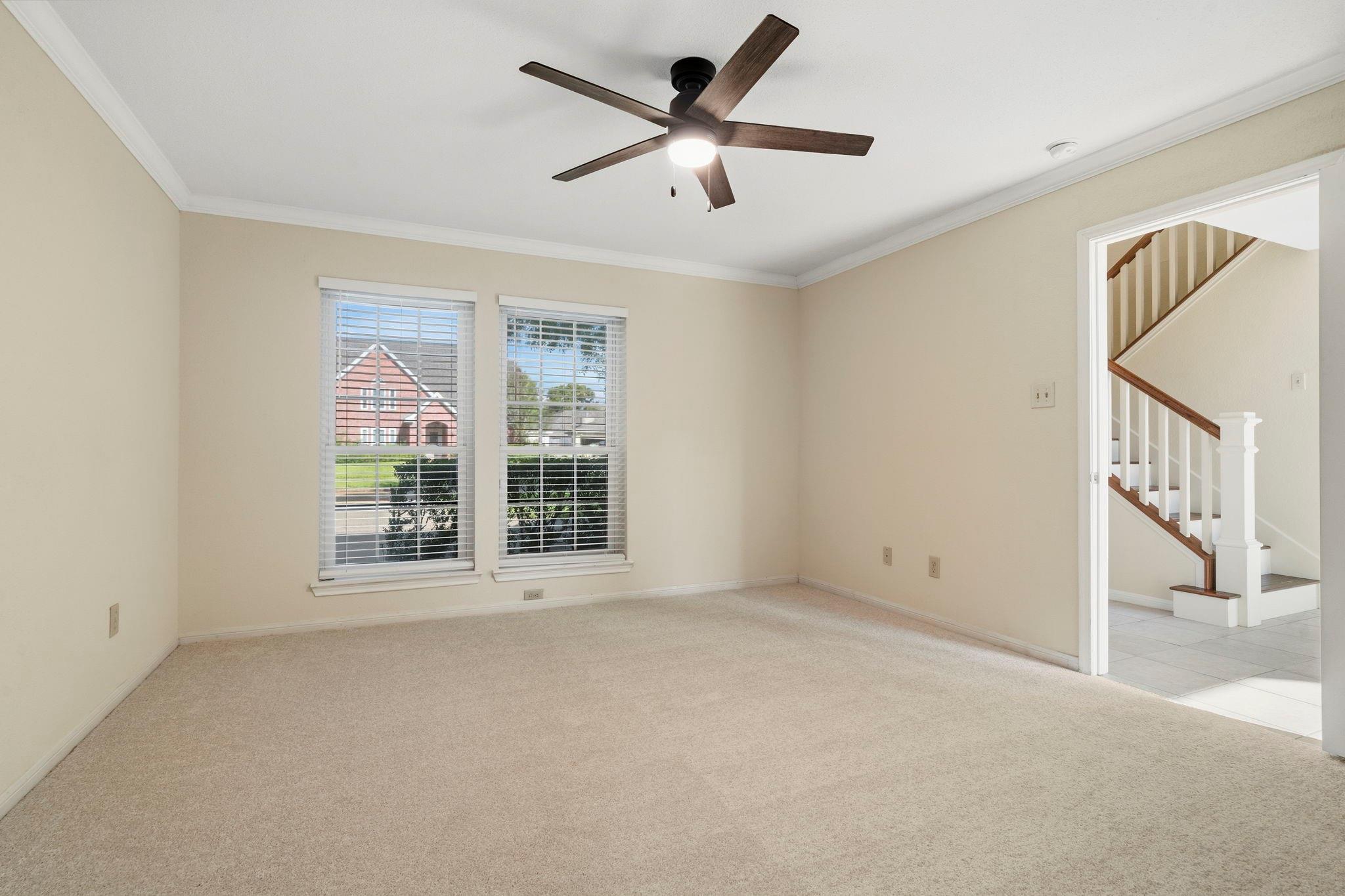 Vacant carpeted room with two windows, a ceiling fan, and a view of the staircase.