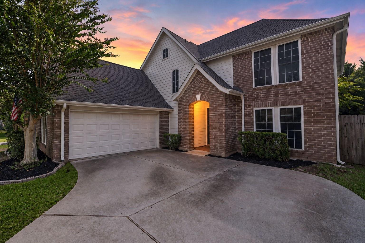 Two-story brick home at dusk with a double garage, curved driveway, and warmly lit entry.