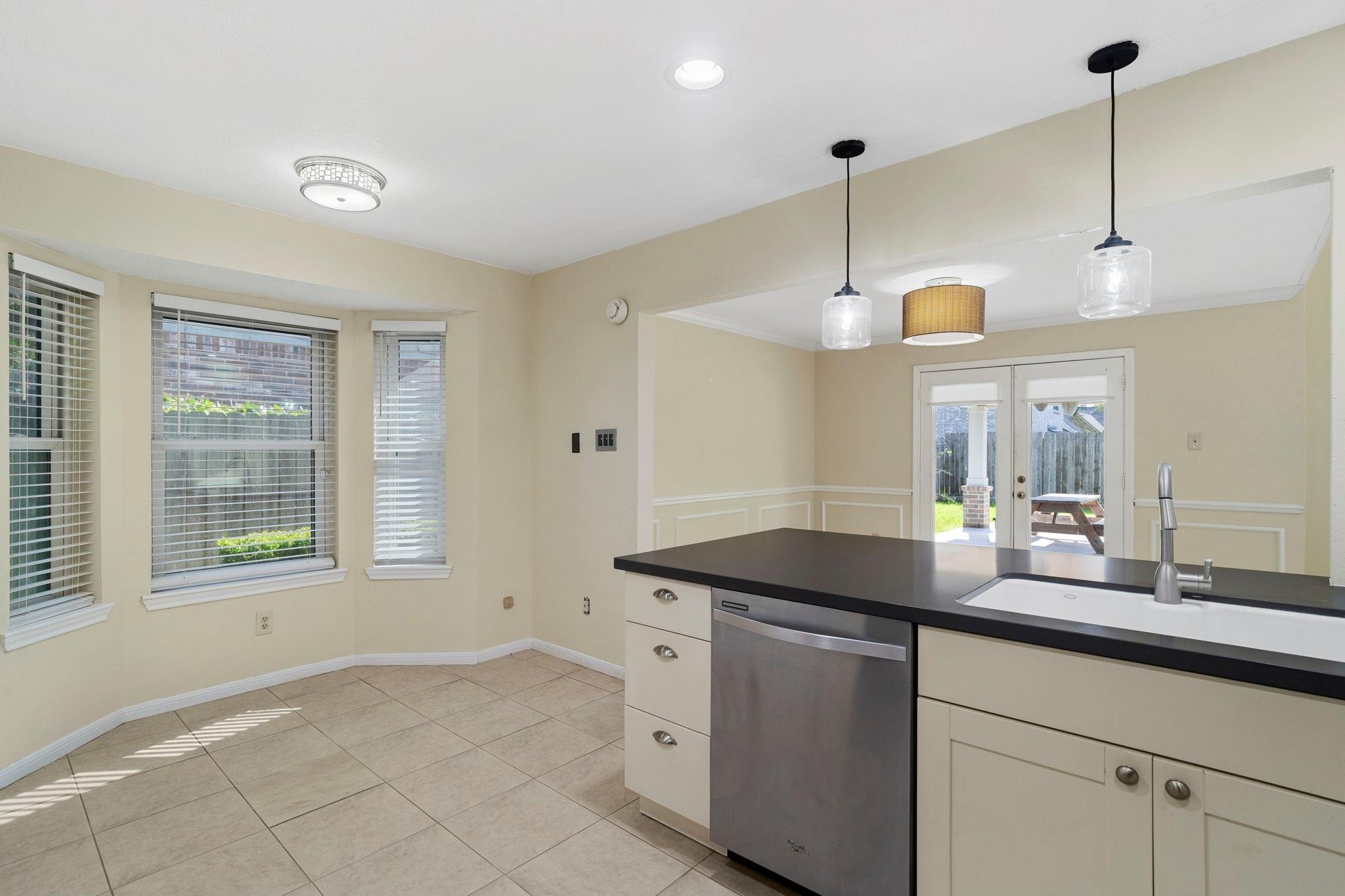Kitchen with a dark island, stainless-steel dishwasher, and French doors opening to a fenced backyard.