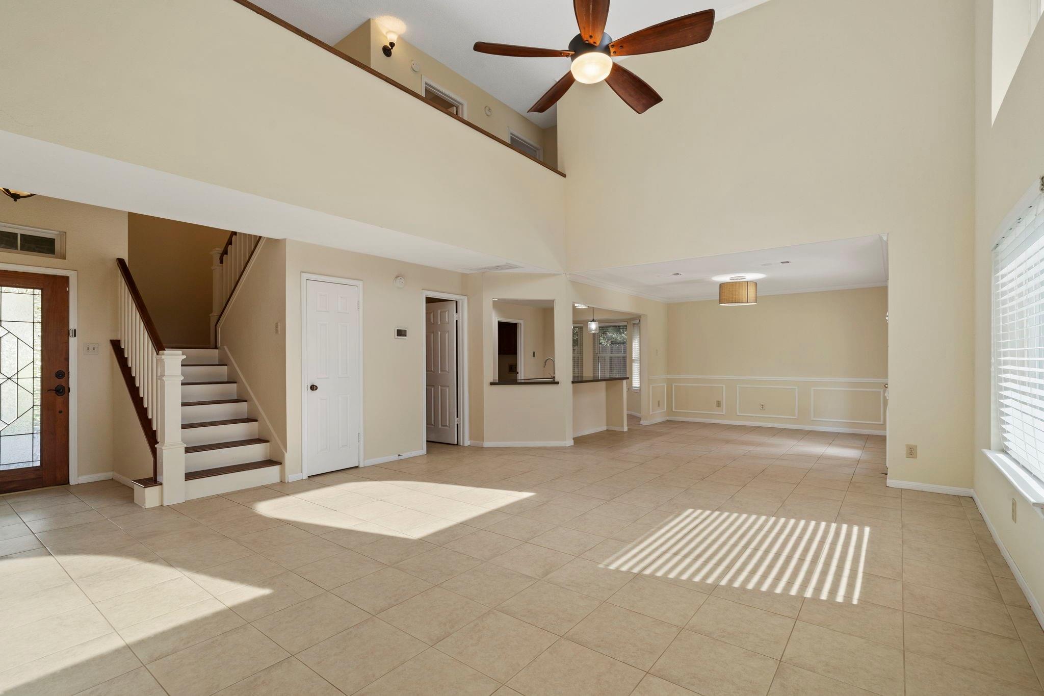 Open-plan living and dining area with tiled floors, a staircase, and a vaulted ceiling with ceiling fan.
