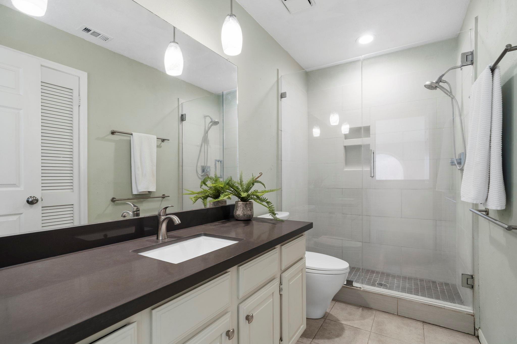 Bathroom with a dark vanity, large mirror, and glass-enclosed tiled shower.