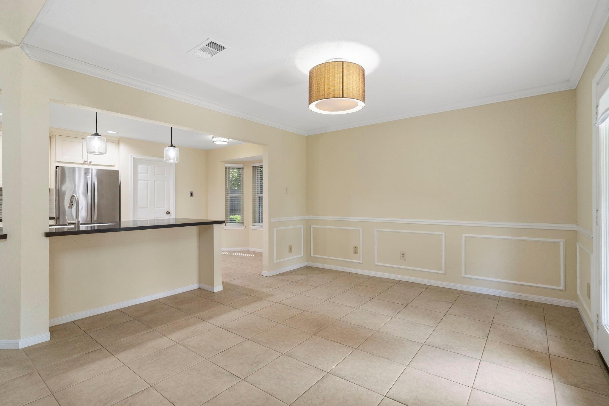 Vacant dining area with tiled floors, paneled walls, and a counter opening to the kitchen.