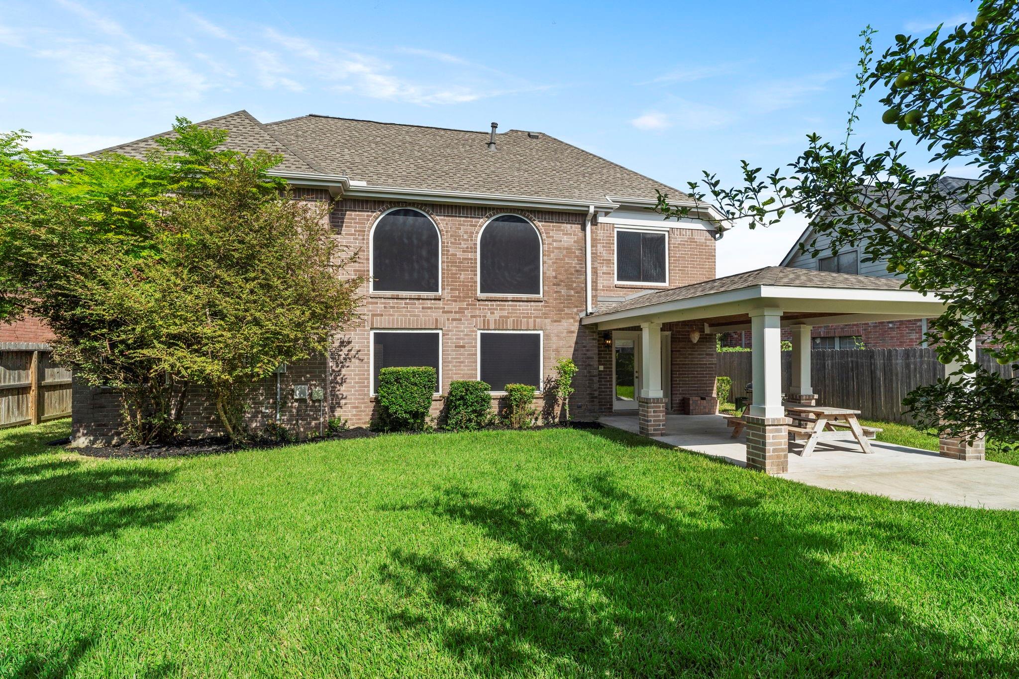 Two-story brick house with arched windows, a covered patio, and a broad green lawn.
