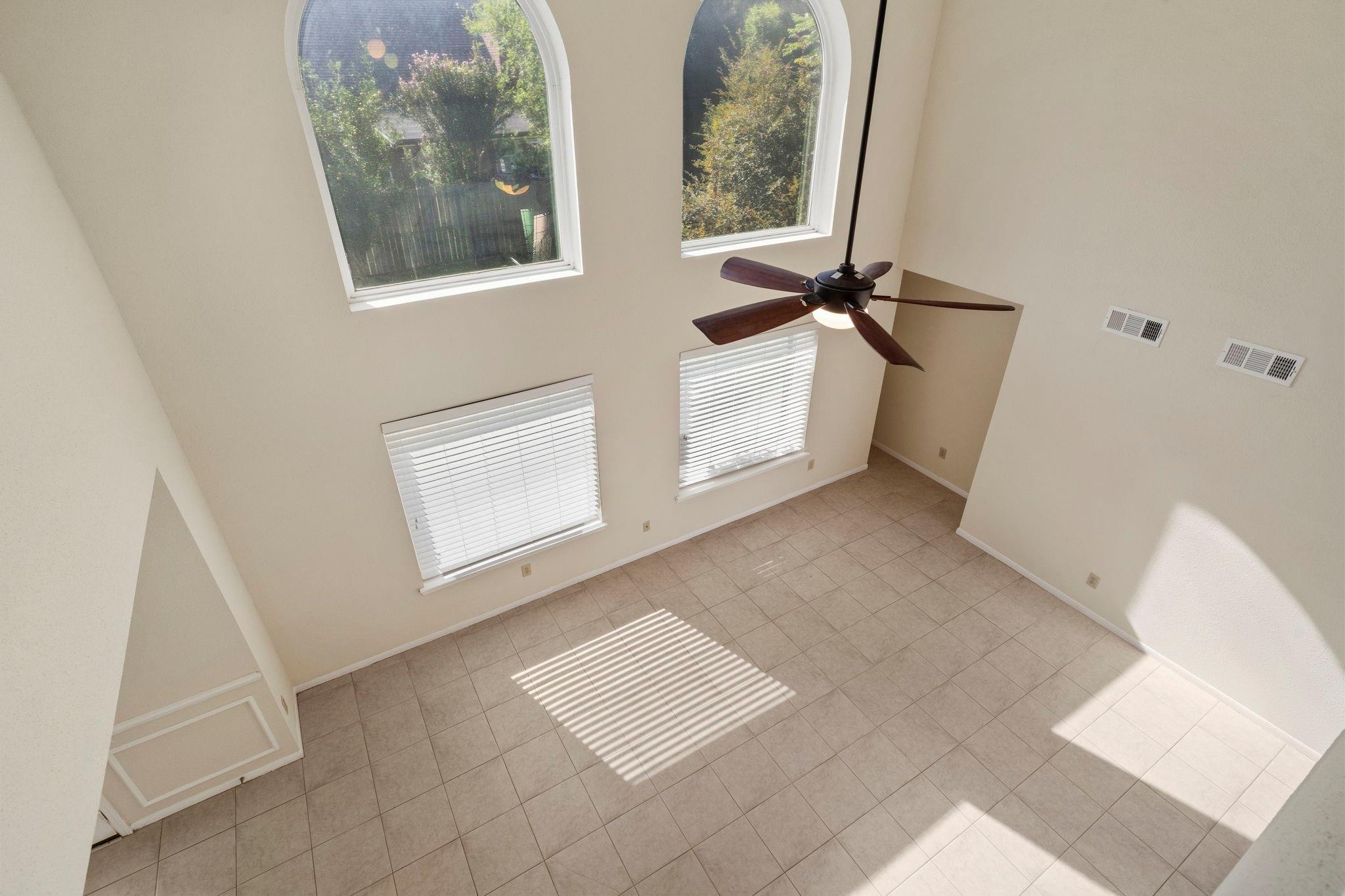 Vacant high-ceilinged room with tiled floor, ceiling fan, and tall arched windows.