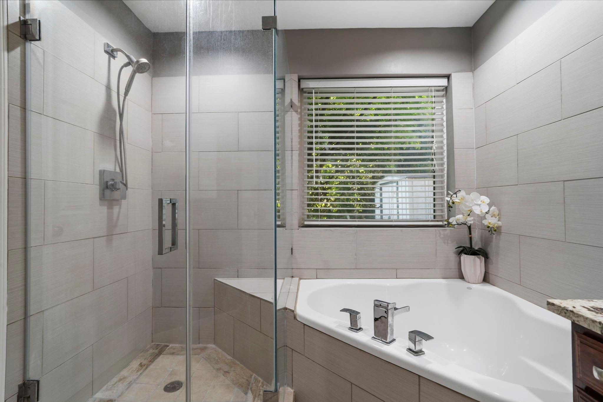 Bathroom with a glass walk-in shower, soaking tub, and window with white blinds.