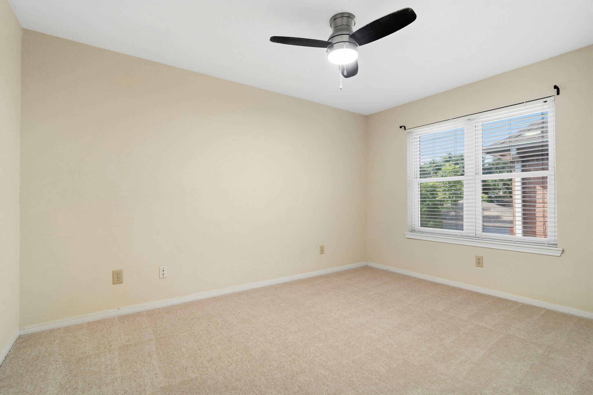 Empty carpeted bedroom with a ceiling fan and a wide window with white blinds.