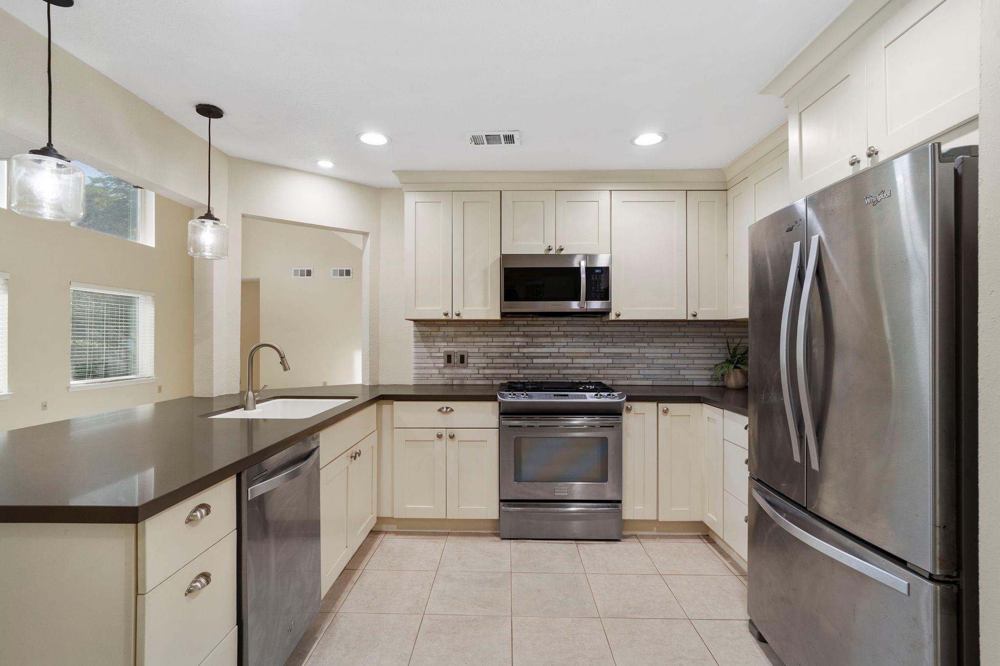 Kitchen with cream cabinets, dark counters, tiled backsplash, and stainless steel appliances.