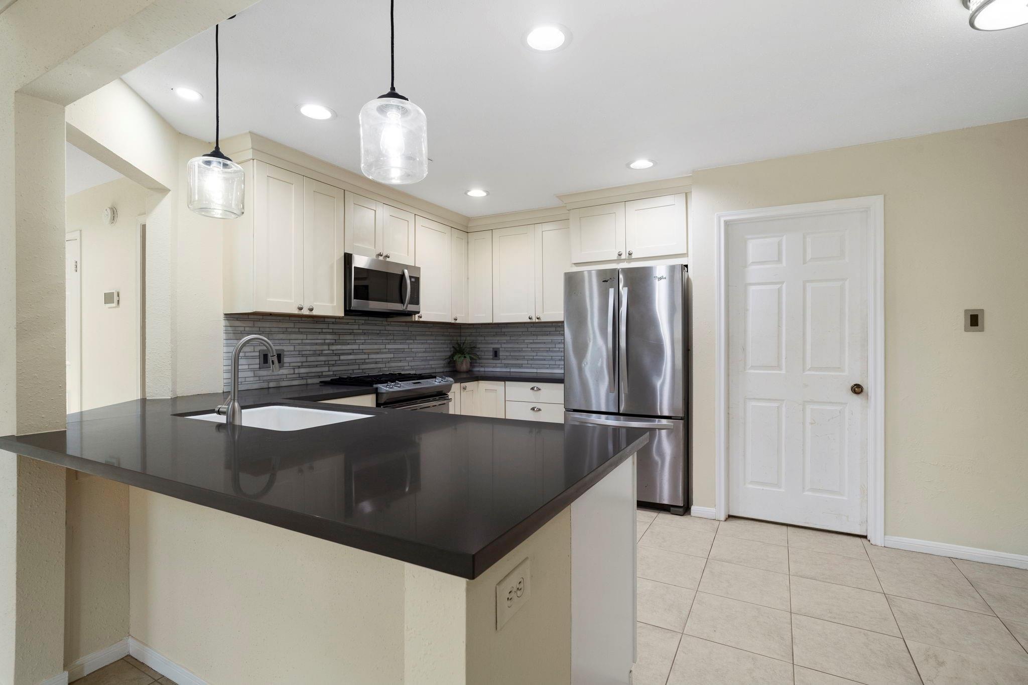 Kitchen with white cabinets, stainless steel appliances, and a large dark island countertop.