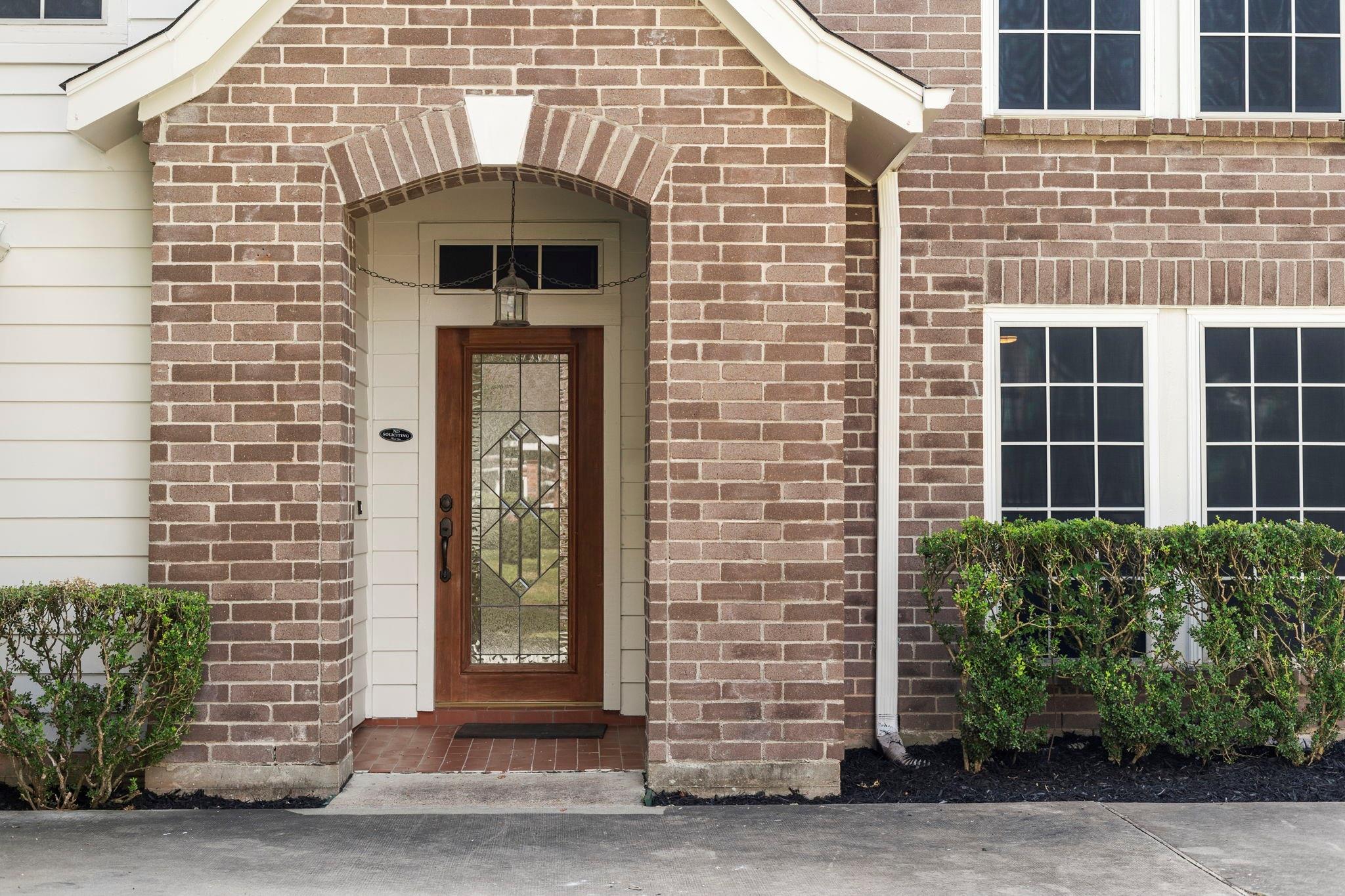 Brick home entrance with a wooden glass-panel door beneath an arched portico.
