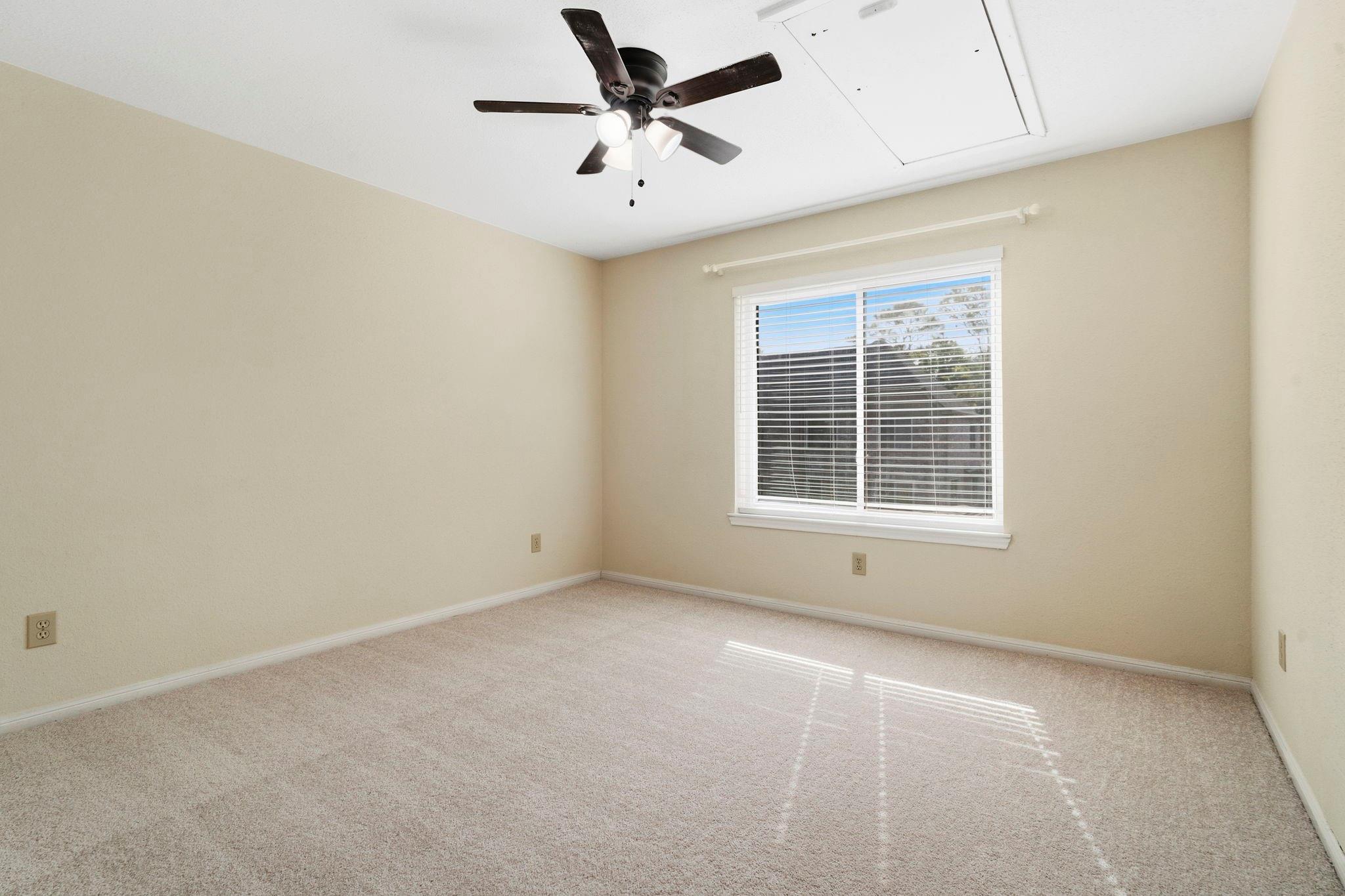 Empty carpeted room with beige walls, a blinded window, and a ceiling fan with lights.