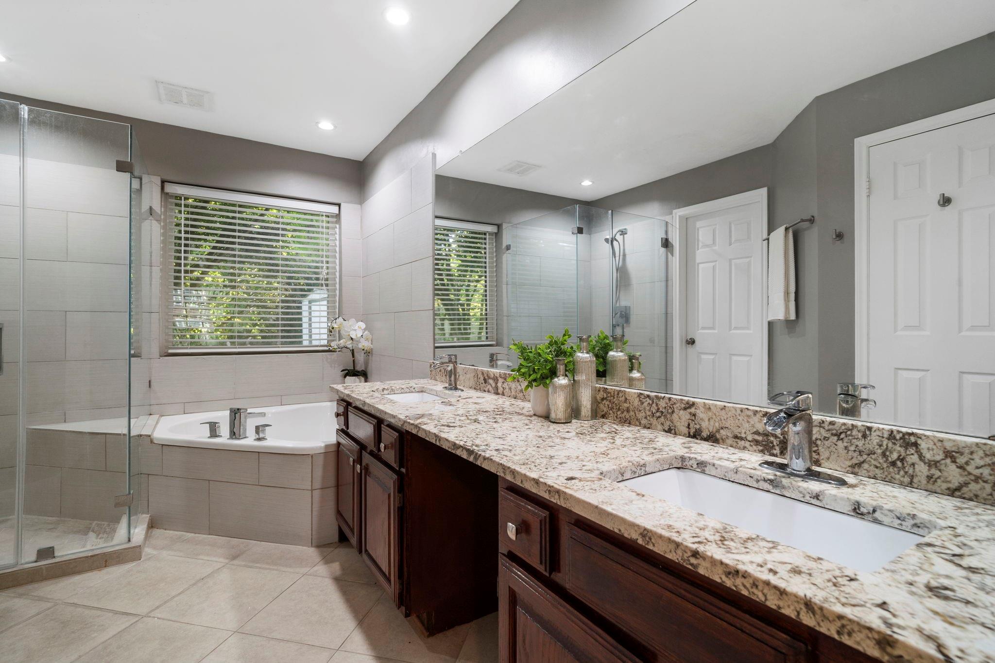 Bathroom with a glass shower, built-in tub, and long granite double-sink vanity.