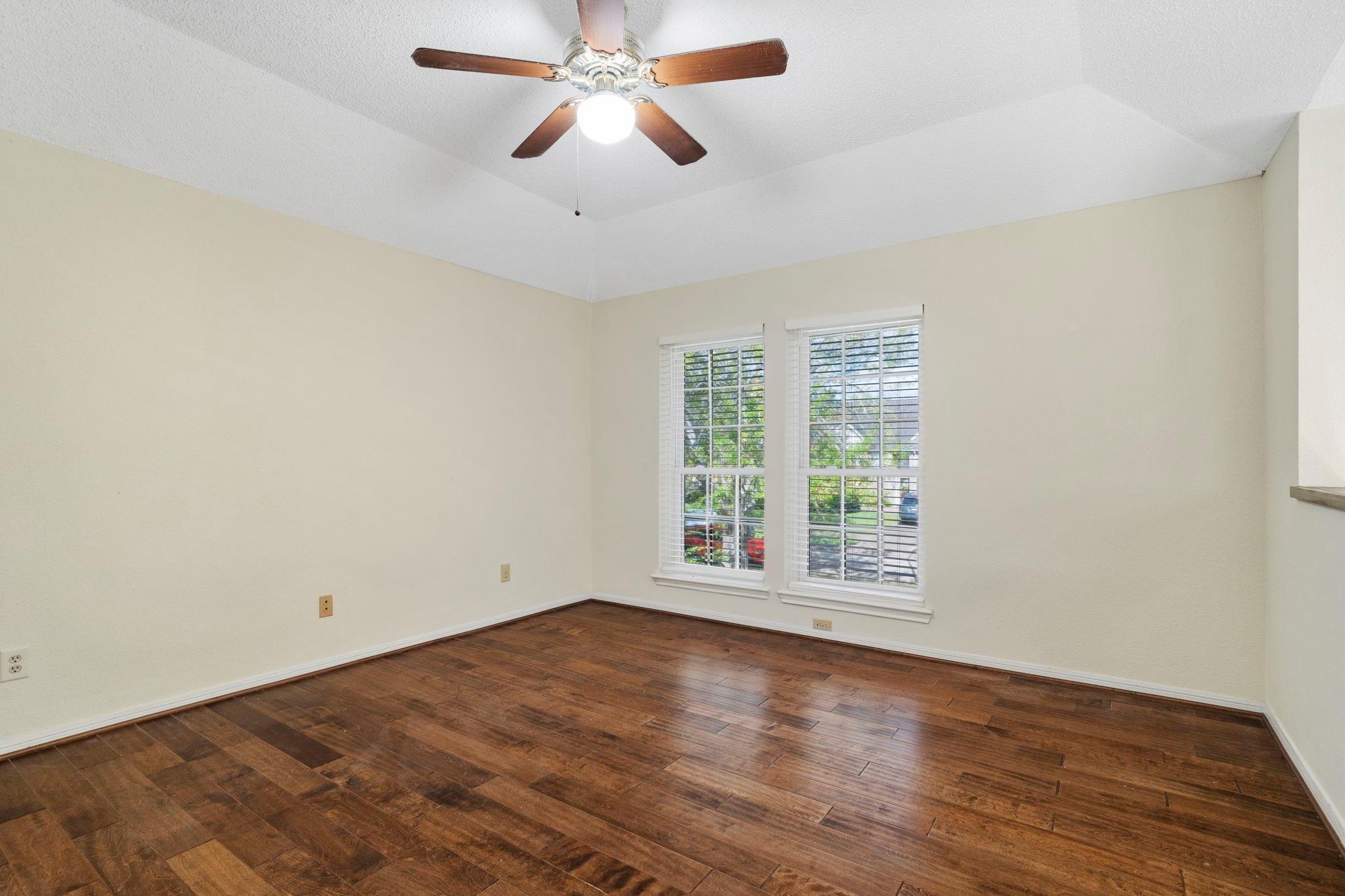 Empty room with dark hardwood floors, two windows with white blinds, and a ceiling fan.