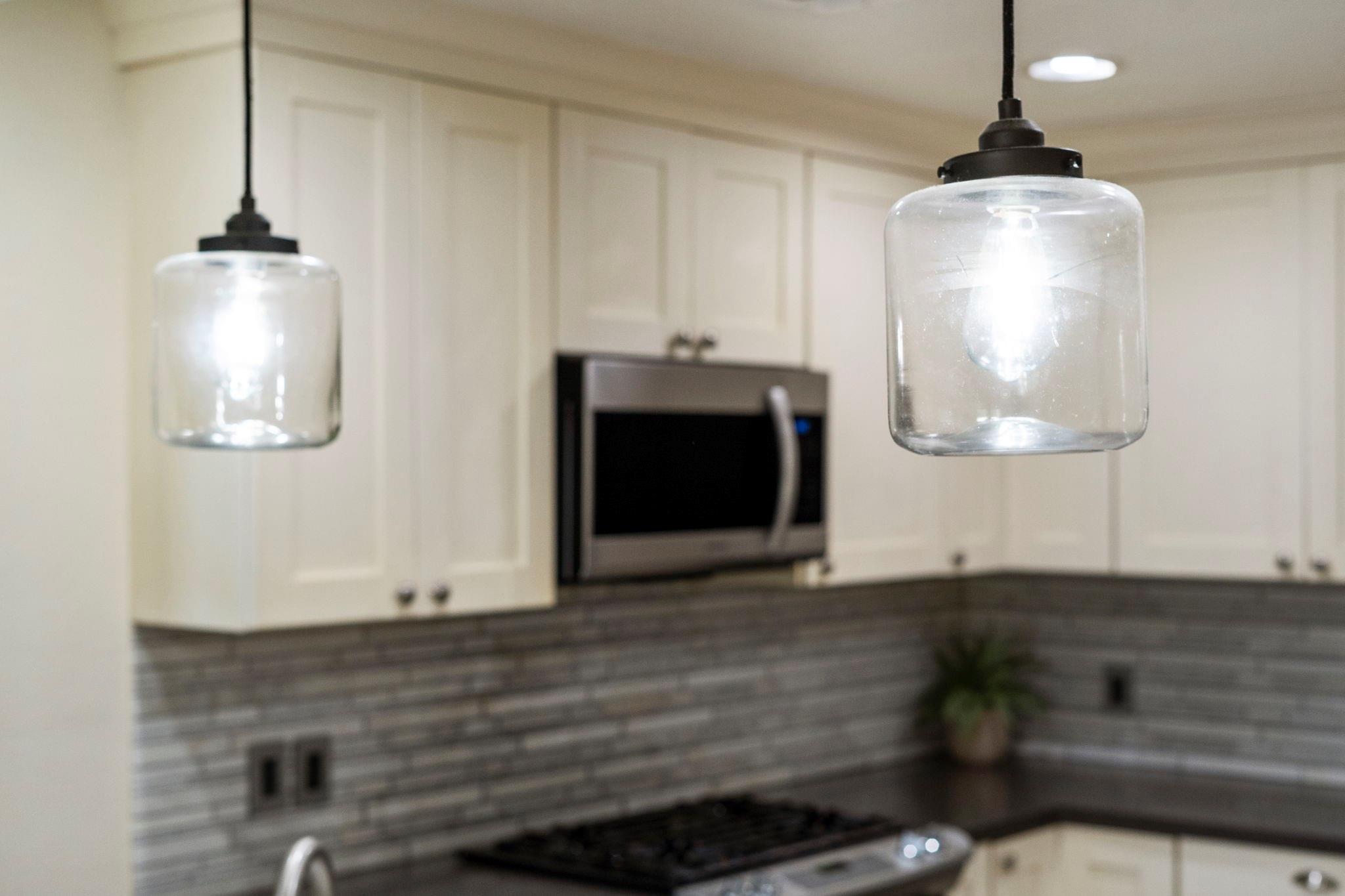Kitchen with white cabinets, gray tile backsplash, stainless microwave, and glass pendant lights.