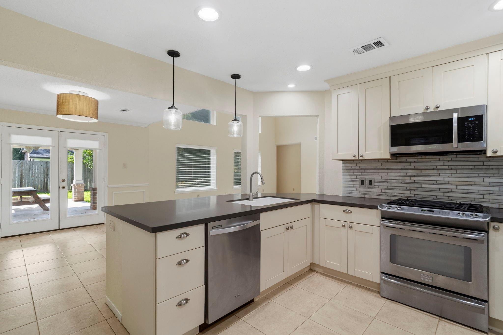 Kitchen with cream cabinets, dark countertops, a sink island, and stainless steel appliances beside patio doors.