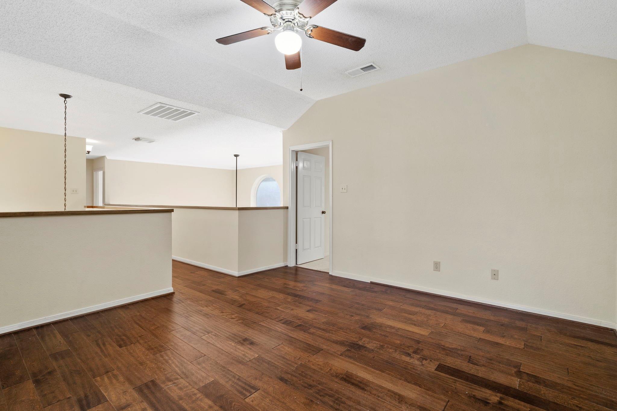 Empty living area with dark hardwood floors, a ceiling fan, and an adjoining open space.