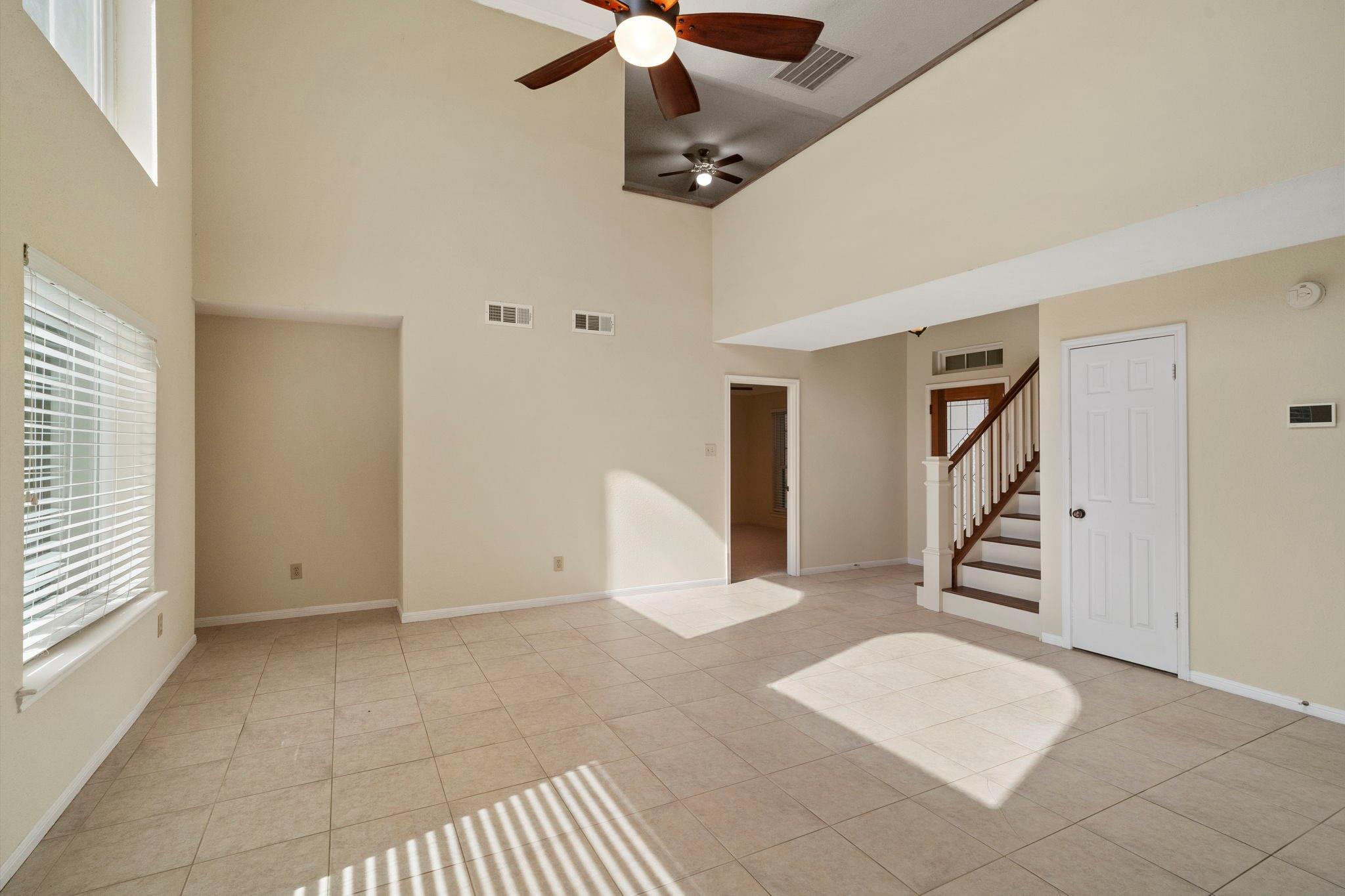 Vacant living room with tiled floors, high ceilings, and a staircase with dark wood accents.