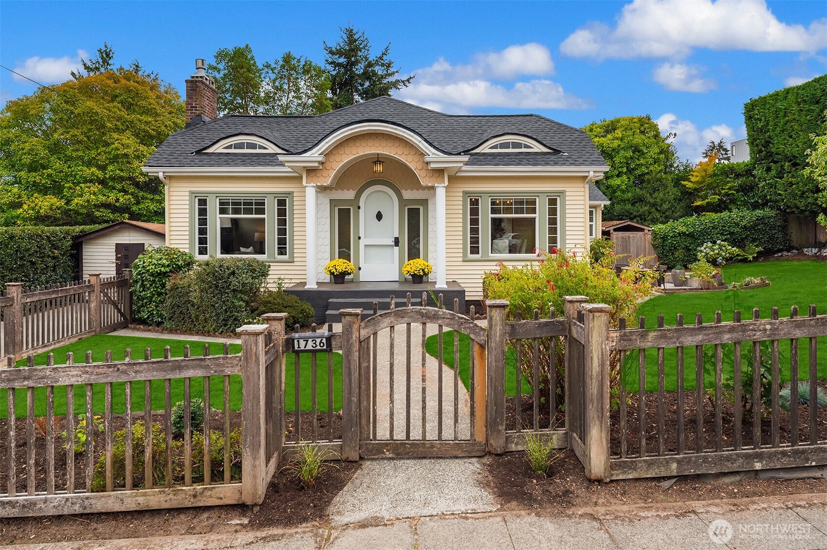 Cream cottage with a curved entry and white door behind a weathered wooden garden gate.