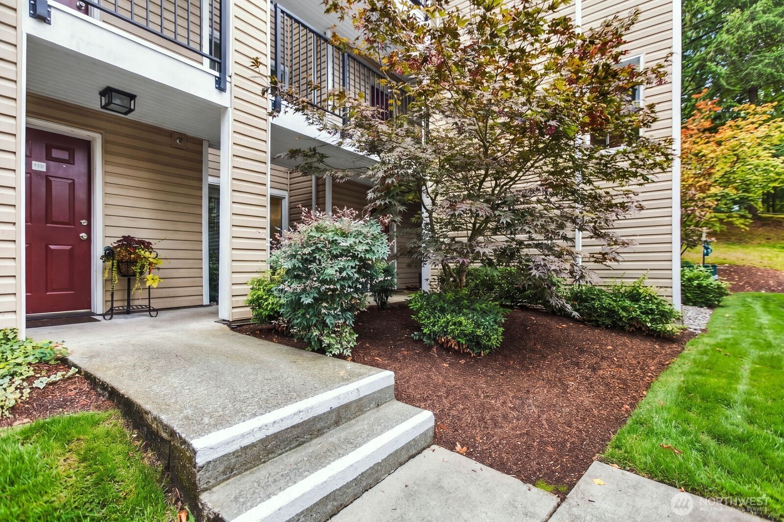 Residence entrance with burgundy door, concrete steps, balconies, and autumn landscaping.