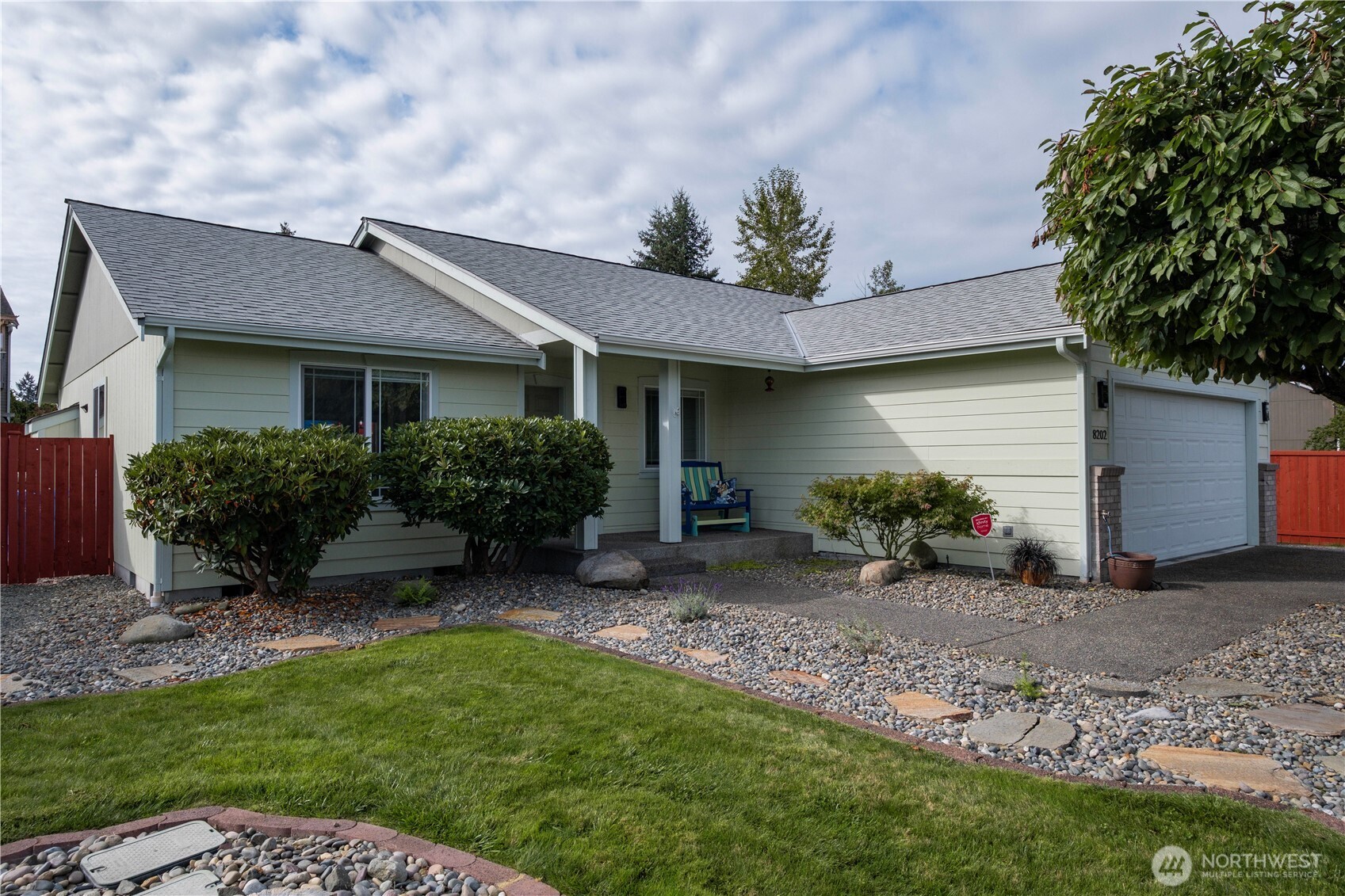 Pale green single-story house with an attached garage, covered entry, and landscaped front yard.
