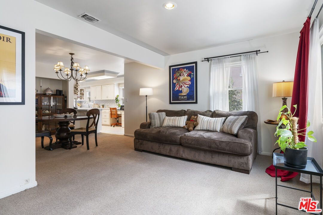 Living room with a brown sectional, adjacent dining area, and view into the white kitchen.