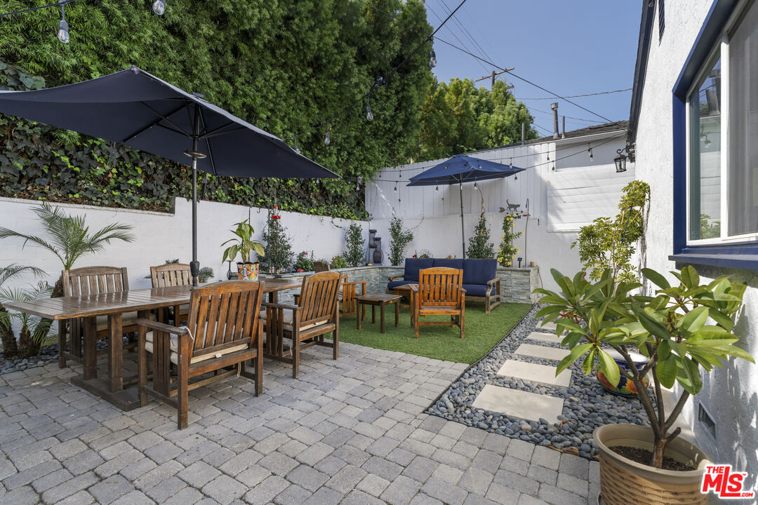 Outdoor patio with wooden dining and lounge seating, navy umbrellas, and a green turf area.