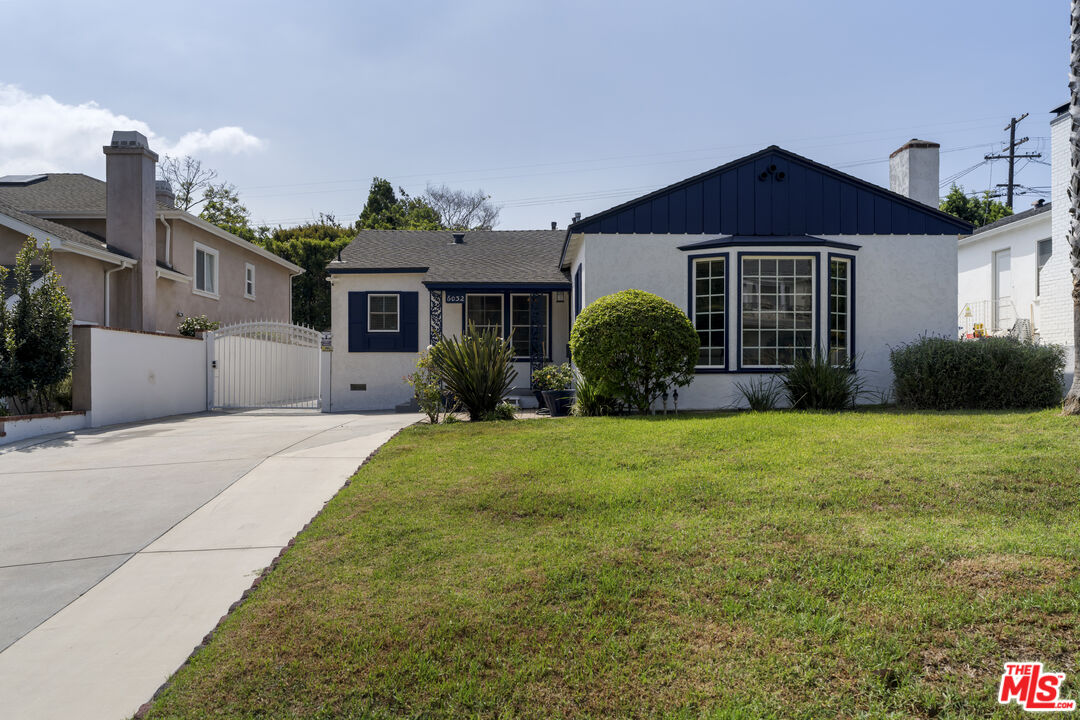 White single-story home with navy trim, a large bay window, front lawn, and gated driveway.